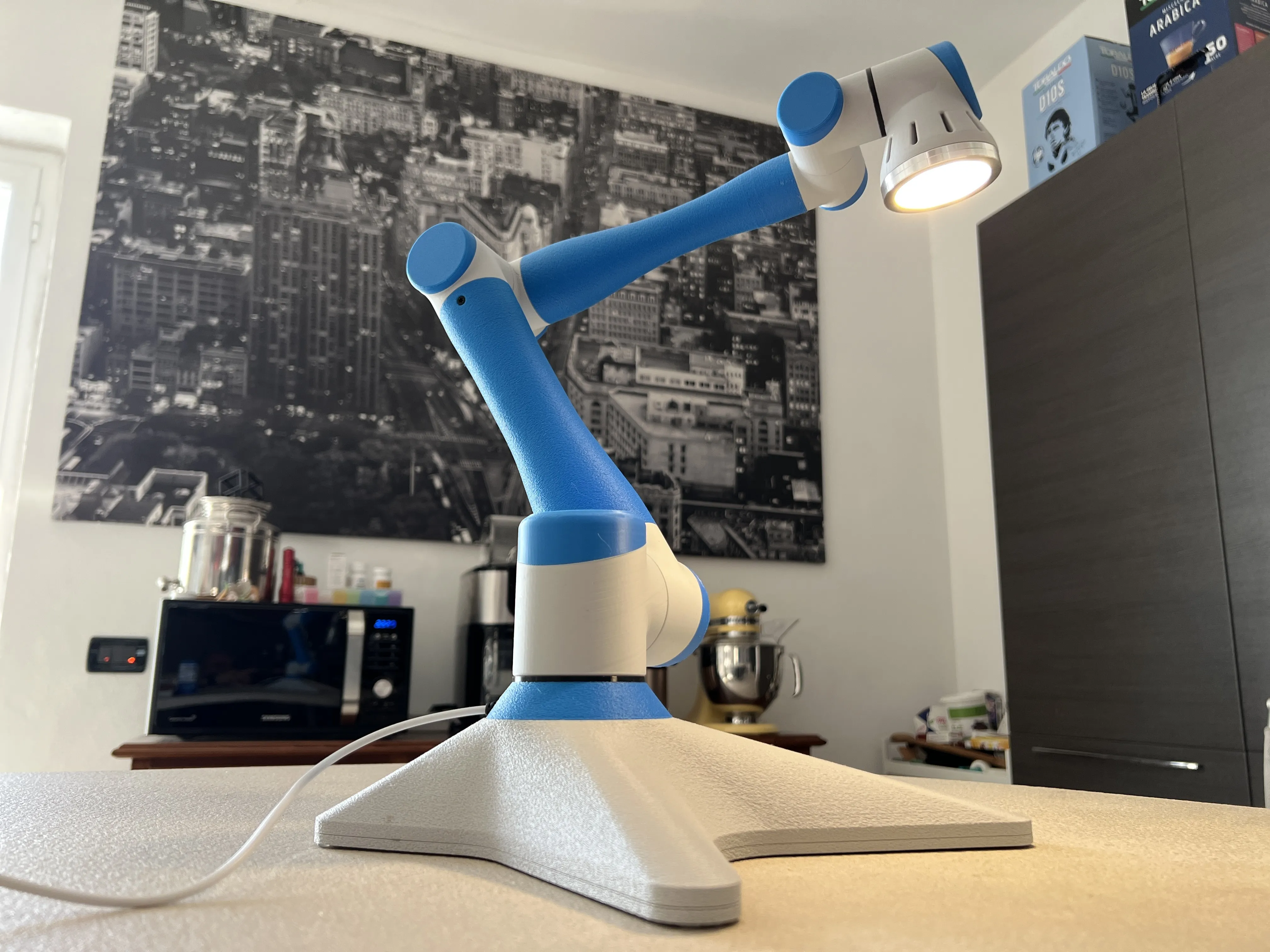 3D-printed articulated desk lamp styled like an industrial robot arm, in blue and white, with a lit LED head